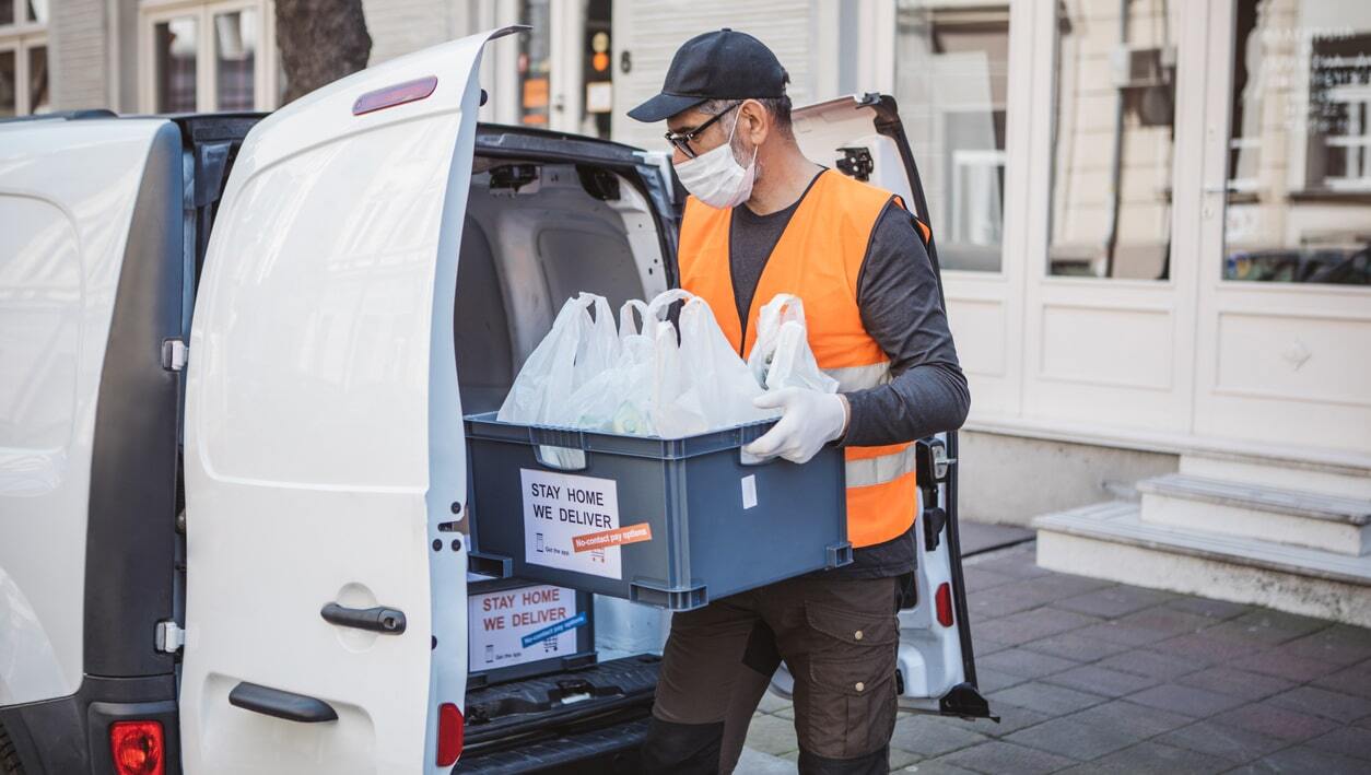 Delivery driver loading packages in a delivery van, preparing for contactless delivery during the pandemic.