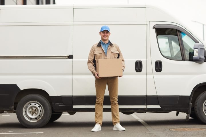 Delivery driver next to a delivery van preparing to drop off or deliver a package at a customer shipping address