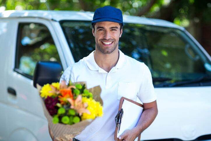Flower delivery driver standing in front of a delivery car delivering a flower bouquet from a local florist