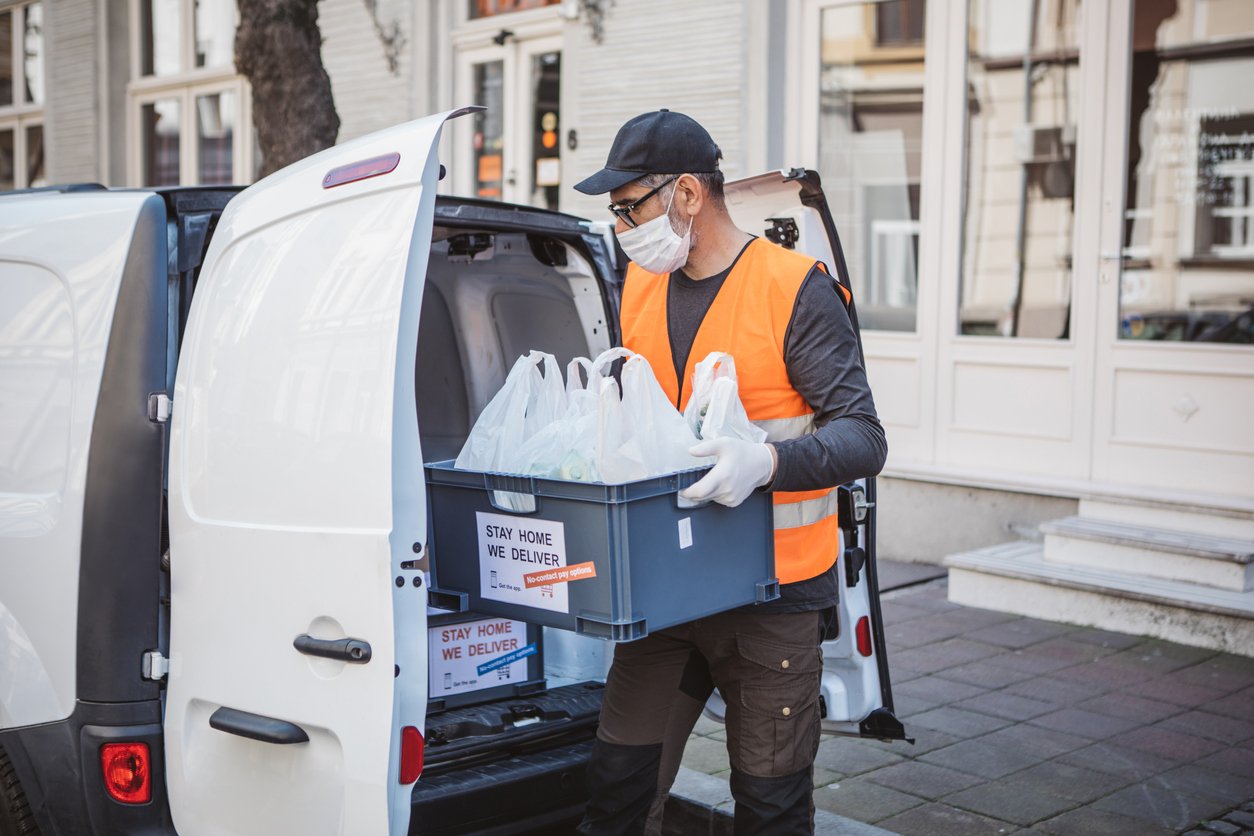 Delivery driver delivering box with groceries and fresh food ordered online during quarantine. Stay home we deliver sign on box.